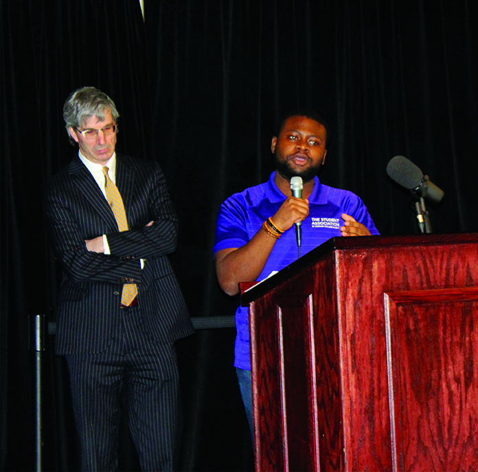 Meri Kim Oliver, vice-president of student affairs standing behind former Student Association interim president Vianney Nengue who is talking at the podium.